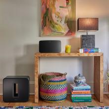 Sonos Sub Gen 4 in black on the floor beside a side table with a speaker and lamp