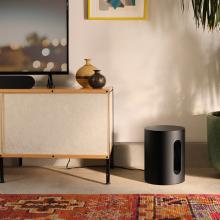 SONOS Sub Mini in black on the florr beside a sideboard in a living room