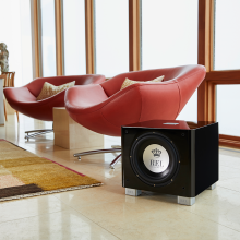 REL T/9x Sub-woofer in black on the floor beside two large chairs