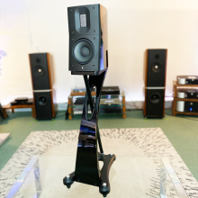 Raidho Acoustics TD1.2 Speaker in black on a glass table in the ripcaster showroom with other HiFi equipment in the background including Kudos 808 speakers and a Linn LP12.