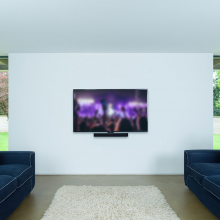 Flexson Adjustable Wall Mount Beam x1 fixed to a wall with a Sonos Beam in place and a TV above.  Fixed on a light coloured wall with a navy sofa either side  The sofas are facing each other.