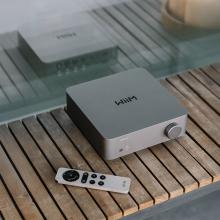 WiiM Vibelink Amp on a wooden shelf with a remote control beside it