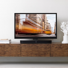 Flexson Adjustable TV Stand Playbase x1 in black with a Playbase and TV on a wooden cabinet.
